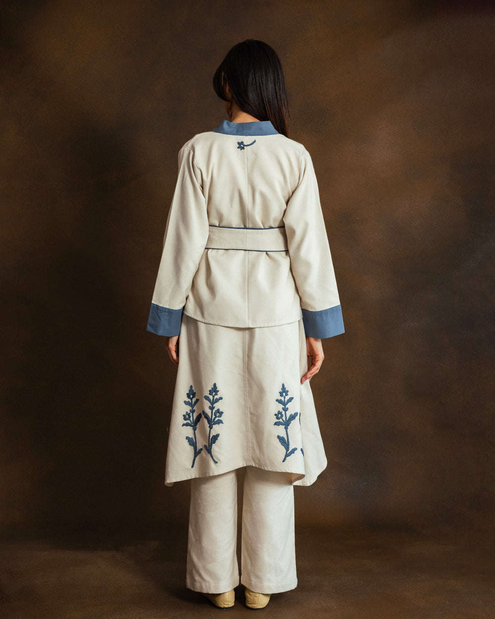 Model wearing a cream wool-blend kimono jacket with blue gabardine trim, matching belt and trousers, front view.