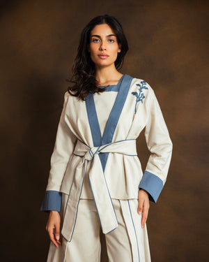 Close-up of cream wool-blend kimono jacket showing blue gabardine trim and subtle floral detailing.