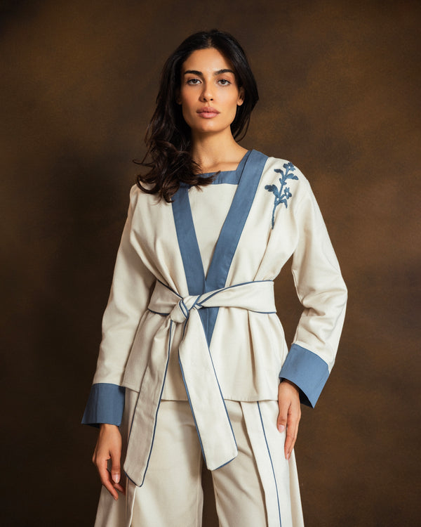 Close-up of cream wool-blend kimono jacket showing blue gabardine trim and subtle floral detailing.
