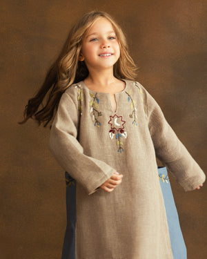 Close-up of hand-embroidered floral motifs and a crescent moon inspired by Ramadan nights on a girls' beige raffia linen kaftan.