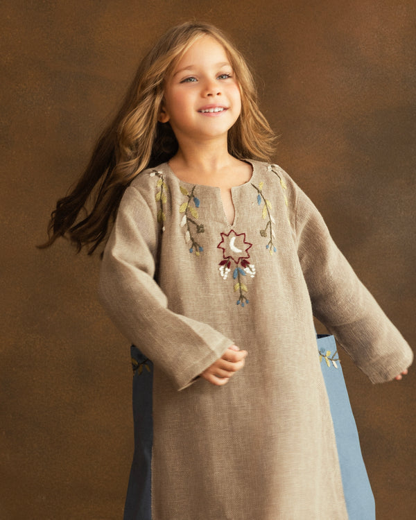 Close-up of hand-embroidered floral motifs and a crescent moon inspired by Ramadan nights on a girls' beige raffia linen kaftan.
