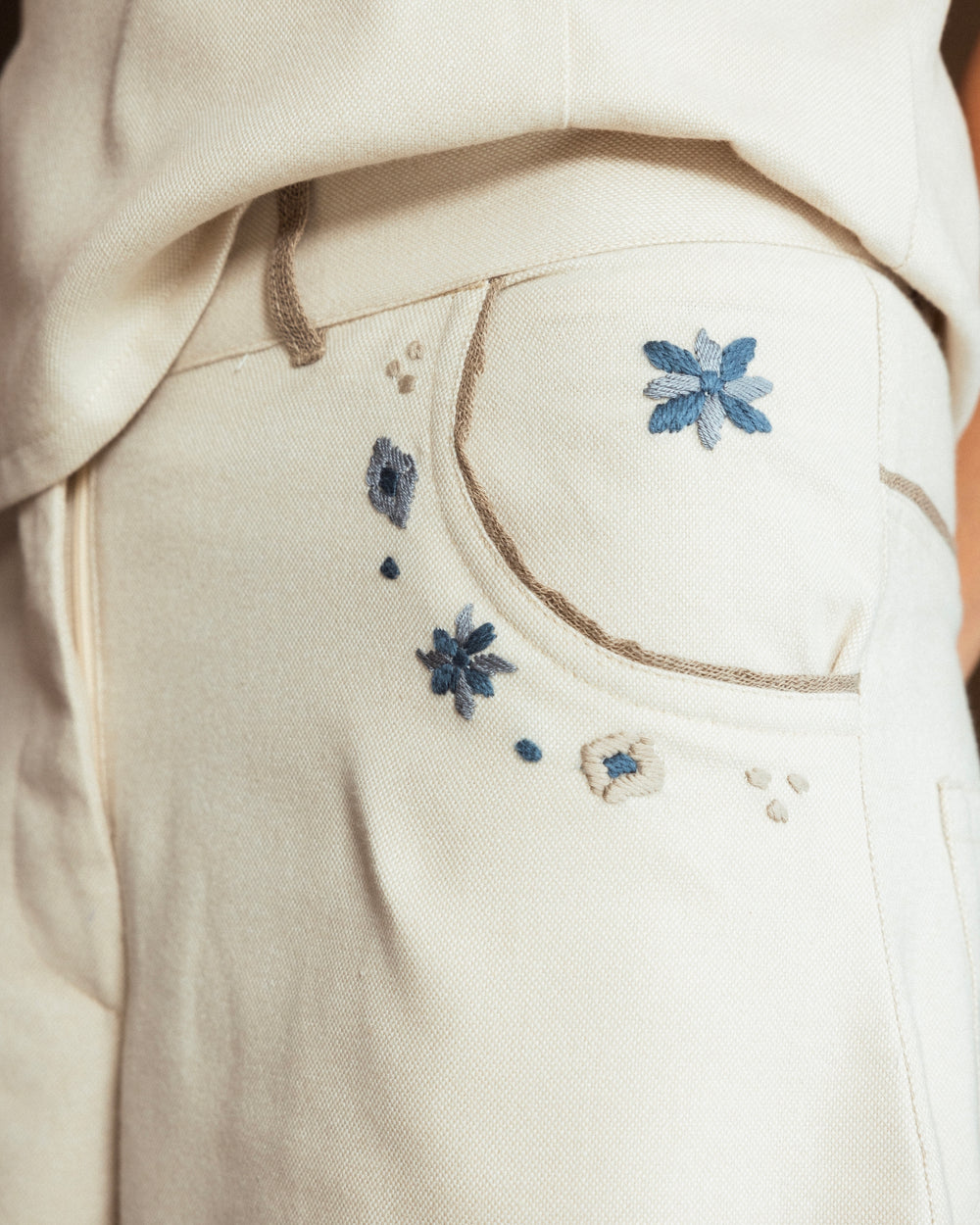 Model wearing cream wool-blend Mosaico Bubble Pants with hand-embroidered mosaic detailing and raffia trim along the pockets.