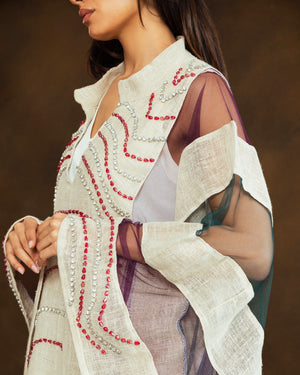 A close-up of a model wearing a cream-colored embroidered vest over sheer purple sleeves, featuring red and silver beadwork details.