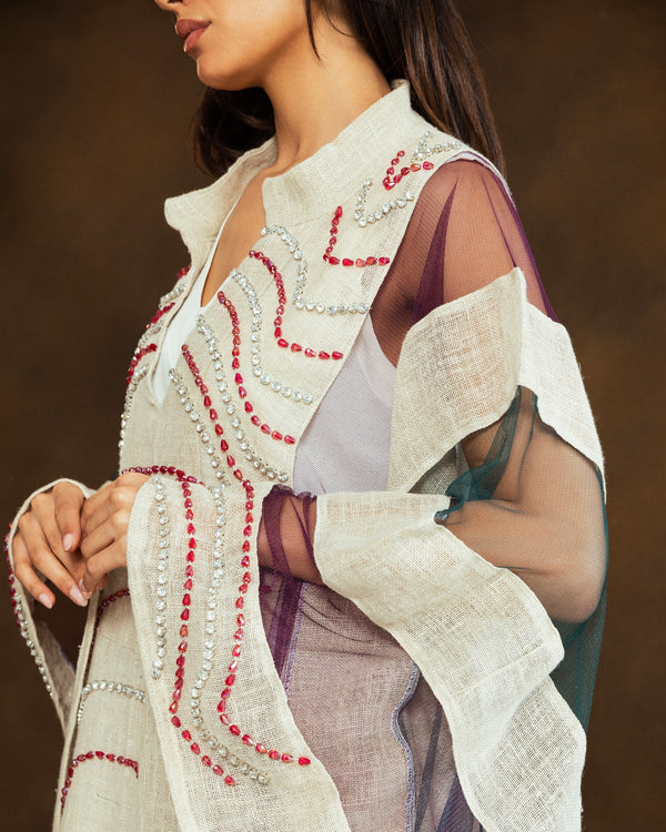 A close-up of a model wearing a cream-colored embroidered vest over sheer purple sleeves, featuring red and silver beadwork details.