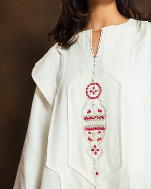 A close-up of a model wearing a white linen kaftan top with intricate red and silver beaded hand-embroidery on the front neckline.