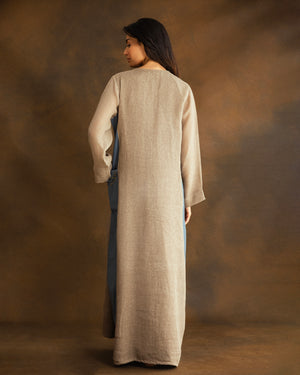 Back view of a beige raffia linen kaftan with contrasting dusty blue gabardine side panels and a relaxed, floor-length silhouette.
