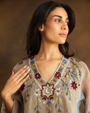 Close-up of intricate hand-embroidered floral detailing and a crescent moon motif inspired by Ramadan nights on a beige raffia linen kaftan.